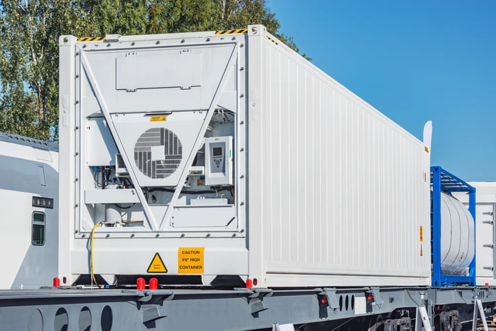 A refrigerated container being transported on the back of a flat bed truck.